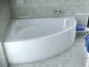 A white corner bathtub with a curved front panel, set against a tiled wall and floor.