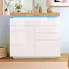 A white high-gloss sideboard with LED lighting is displayed in a room setting, with decorative items on top and a basket to the side. Podgląd zdjęcia produktu
