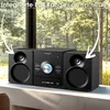 A black stereo system with speakers is placed on a windowsill with a blurred background of trees and foliage. Produktbild-Vorschau