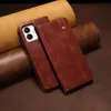 A brown leather phone case is displayed on a textured brown surface, with rolled leather pieces in the background. Produktbild-Vorschau