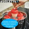 A hand is holding a red egg poacher with an egg inside, which is placed in a pot of boiling water. Produktbild-Vorschau