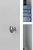 A close-up of a silver cabinet knob on a white cabinet door, with stacked blue towels visible in the background. Náhled obrázku produktu