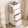 A white bathroom cabinet with drawers and compartments for cosmetics, placed next to a floor lamp and curtains. Produktbild-Vorschau