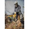 A man wearing protective gear is using a yellow and black DeWalt chainsaw to cut a tree branch on the ground. Voir les images du produit