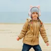 A young girl wearing headphones with cat ears is standing on a beach and listening to music. Náhľad obrázku produktu