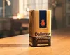 A package of Dallmayr prodomo coffee sits on a wooden table in a warm, indoor setting. Podgląd zdjęcia produktu