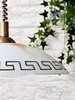 A close-up of a pendant lamp with a Greek key pattern, hanging in front of a brick wall with ivy. Podgląd zdjęcia produktu