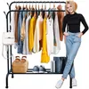A woman stands next to a clothing rack filled with clothes, with accessories on the bottom shelf. Anteprima dell’immagine prodotto