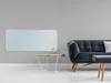 A modern living room scene with a white glass heater mounted on a gray wall, next to a dark gray sofa and a small wooden side table. Produktbild-Vorschau