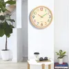 A wall clock is displayed on a white wall next to a potted plant and a small table with a coffee cup and sunglasses. Produktbild-Vorschau