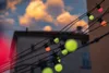 String lights with colorful bulbs are strung across the foreground, with a building and cloudy sky in the background. Náhled obrázku produktu
