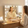 A woman is applying makeup in front of a lighted vanity mirror. Podgląd zdjęcia produktu