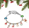 A Christmas-themed charm bracelet with various holiday-themed charms, set against a backdrop of fir branches and holly berries. Produktbild-Vorschau
