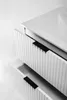 A close-up, high-angle view of a white bathroom vanity with two drawers, showing the ribbed texture of the drawer fronts and black handles. The top of the vanity, which appears to be a countertop with a sink basin, is also visible. Voir les images du produit