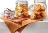 Three glass jars are arranged on a brown cloth. One jar contains pickled vegetables, another contains cookies, and the third contains salt and spices. Two red chili peppers are also visible. Produktbild-Vorschau