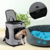 A dog is peeking out of a gray pet carrier backpack next to a gray pet bed with a blue cushion. Anteprima dell’immagine prodotto