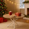A cozy Christmas scene with a round wooden table in the foreground, featuring a mug of hot chocolate, cookies, and a gift box. A decorated Christmas tree is on the left, and a fireplace with garland is on the right. Náhľad obrázku produktu