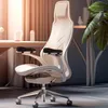 A close-up shot of a modern white ergonomic office chair with black armrest pads, set in a softly lit room with a blurred background. Náhled obrázku produktu