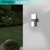 An outdoor motion-sensing light fixture mounted on a brick wall, with a garden in the background. Produktbild-Vorschau