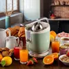 A breakfast scene with a green juicer, croissants, juice, and fruit. Produktbild-Vorschau