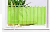 A sheer green curtain hangs in a window, with a plant visible behind it. Produktbild-Vorschau