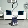 A blue vacuum cleaner is shown in a living room setting with a white sofa and teal cushions. Produktbild-Vorschau