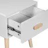 A close-up view of an open drawer on a white nightstand with wooden legs. Podgląd zdjęcia produktu