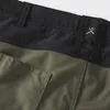 A close-up view of the waistband and pocket of a pair of green shorts, featuring a textured black waistband with a silver logo. Podgląd zdjęcia produktu