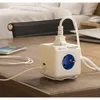 A white PowerCube extended USB power strip is shown on a wooden desk, plugged into a wall outlet, with a phone charging next to it. Produktbild-Vorschau