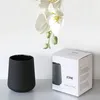 A black ceramic mug and its packaging are displayed next to a white orchid. Produktbild-Vorschau