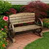 A wooden bench with wagon wheels as armrests is placed in a garden setting with flowers and greenery. Produktbild-Vorschau
