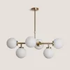 A modern chandelier with a gold metal frame and six white glass globes, suspended against a plain light gray background. Produktbild-Vorschau