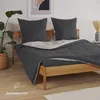 A bed with dark gray bedding and pillows in a room. Voir les images du produit