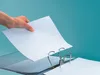 A hand is inserting a sheet of paper into a binder. Produktbild-Vorschau