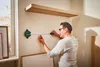 A man is using a digital laser level and tape measure to mark a wall. Produktbild-Vorschau