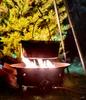 A gas fire pit with a pot hanging over it, set up outdoors at night. Produktbild-Vorschau