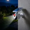 A solar-powered security camera with an LED light is mounted on a textured wall, illuminating a garden path and lawn at night. Produktbild-Vorschau
