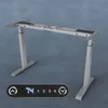 A silver height-adjustable desk frame is shown against a textured gray background. A control panel with a digital display and buttons is in the foreground. Anteprima dell’immagine prodotto