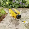 A solar-powered bee decoration sits on a paved garden path, surrounded by plants and flowers. Produktbild-Vorschau