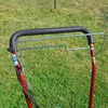 A close-up view of the handle and controls of a red lawnmower, set against a background of green grass. Produktbild-Vorschau