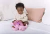 A baby sitting on a bed with a pink plush turtle toy. Podgląd zdjęcia produktu