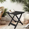 A black folding table is set up on a rug outdoors, surrounded by plants and wicker furniture. Anteprima dell’immagine prodotto