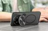 A person's hand is resting on a table next to a smartphone with a case and a magnetic ring. Produktbild-Vorschau