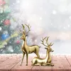 Two golden reindeer figures are displayed on a wooden surface with a blurred Christmas tree and falling snow in the background. Produktbild-Vorschau