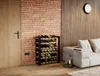 A wine rack filled with bottles is placed next to a sofa in a room with a brick wall and wooden accents. Produktbild-Vorschau