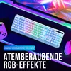 A white gaming keyboard with RGB lighting is shown on a desk with a gaming mouse and controller, with a computer screen in the background displaying colorful lights. Produktbild-Vorschau