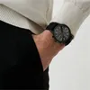 A close-up shot of a person's wrist wearing a black watch. Voir les images du produit