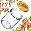 A glass jar and its lid are surrounded by various fresh vegetables and herbs, with a stylized 'K' logo in the upper left corner. Produktbild-Vorschau