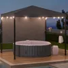 An inflatable hot tub is set up on a wooden deck under a dark gray canopy with string lights, with a small shelf holding drinks and a plant. Náhled obrázku produktu