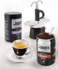 A Bialetti Moka pot, coffee grounds, and a cup of espresso are displayed on a light gray surface. Produktbild-Vorschau
